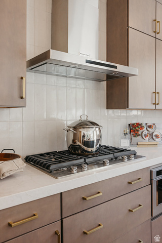 5902 Canyon Rim Road, Unit 620 Lehi, UT 84048 - Photo 9 of 78 Gas cooktop with integrated oven, stainless steel range hood, white tile backsplash, light-toned countertops, and brown cabinetry with brass hardware
