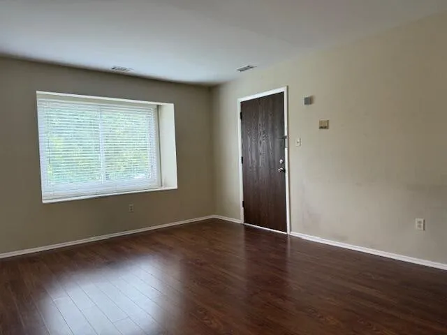 a view of an empty room with wooden floor and a window