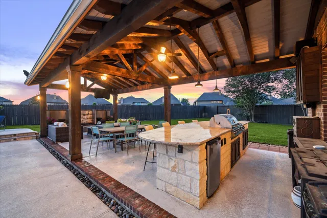 a view of a patio with a table and chairs under an umbrella with a barbeque