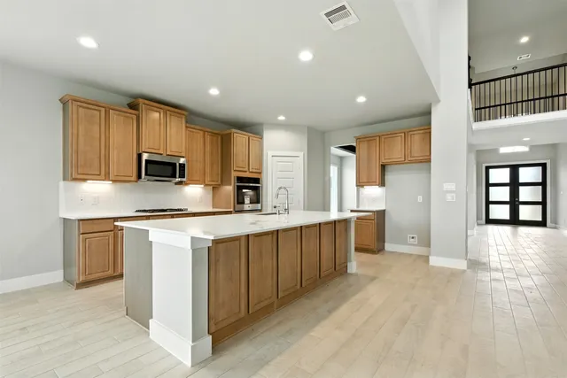 a large kitchen with stainless steel appliances kitchen island granite countertop a stove a sink a refrigerator and white cabinets with wooden floor