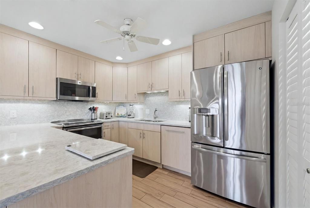 2729 North Beach Road, Unit 211 Englewood, FL 34223 - Photo 19 of 51 a kitchen with stainless steel appliances granite countertop a refrigerator stove a sink and white cabinets with wooden floor