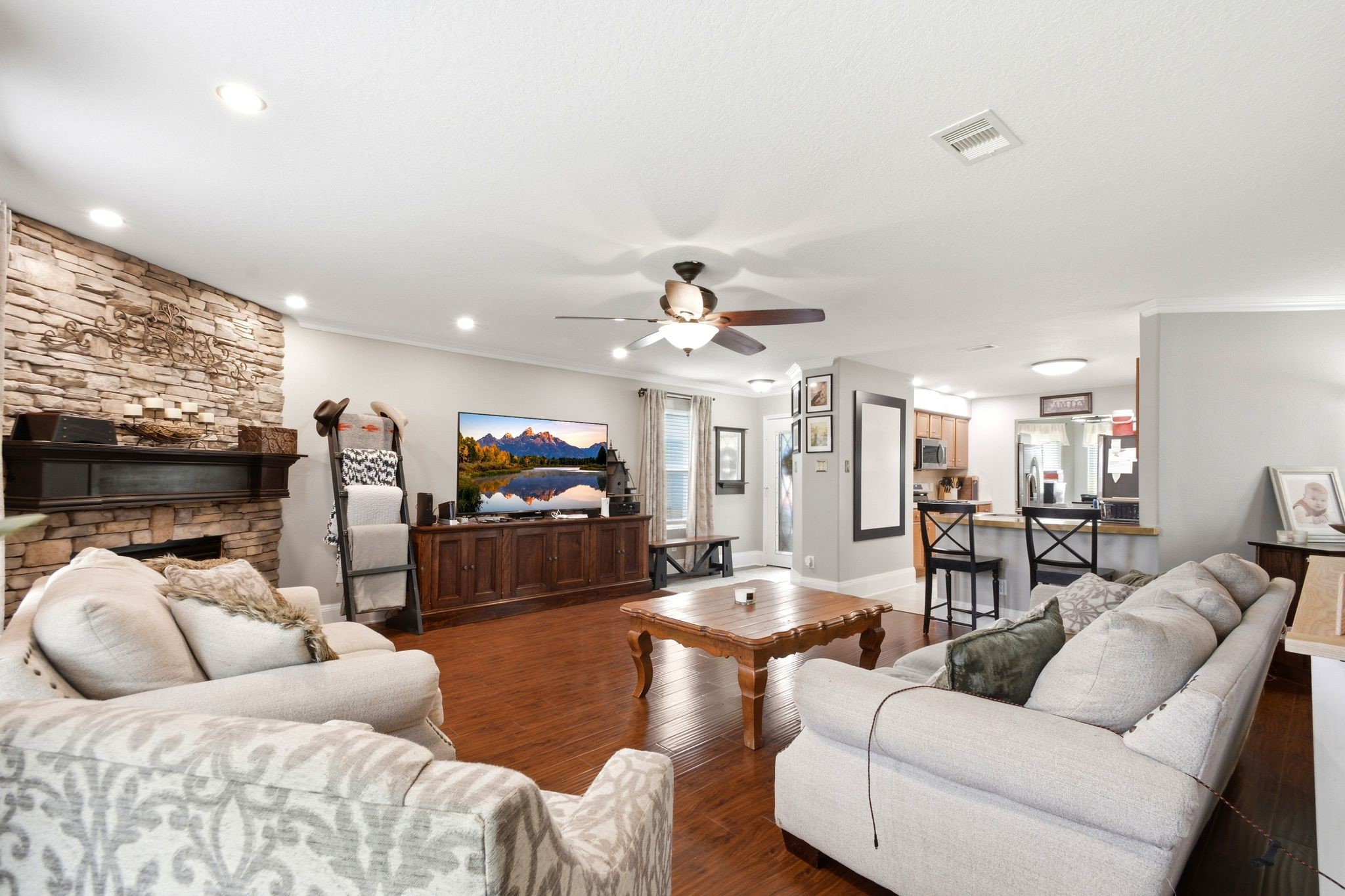 16954 Tableland Trail Conroe, TX 77385 - Photo 8 of 33 Expansive open-concept living room featuring hardwood floors, recessed lighting, a stunning stone fireplace, and direct access to the kitchen with breakfast bar seating. Perfect for entertaining or relaxing with family and friends.