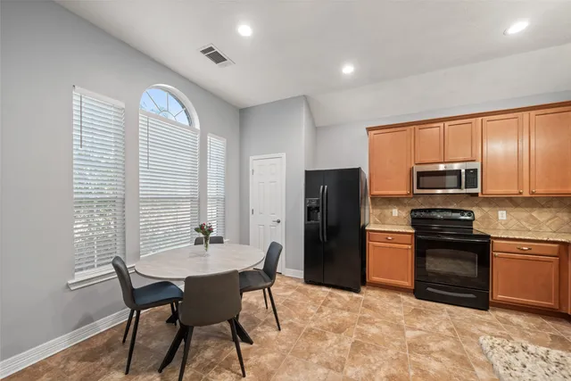 a kitchen with stainless steel appliances granite countertop a stove a refrigerator a sink a dining table and chairs