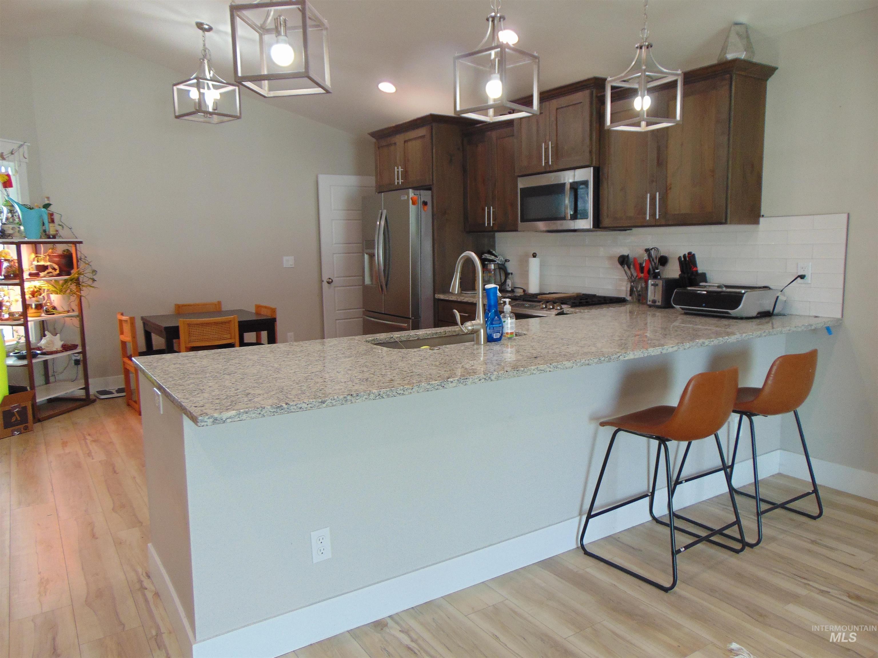 901 Campbell Street Vale, OR 97918 - Photo 6 of 22 Kitchen with a peninsula, light stone counters, light wood-style flooring, stainless steel appliances, and vaulted ceiling