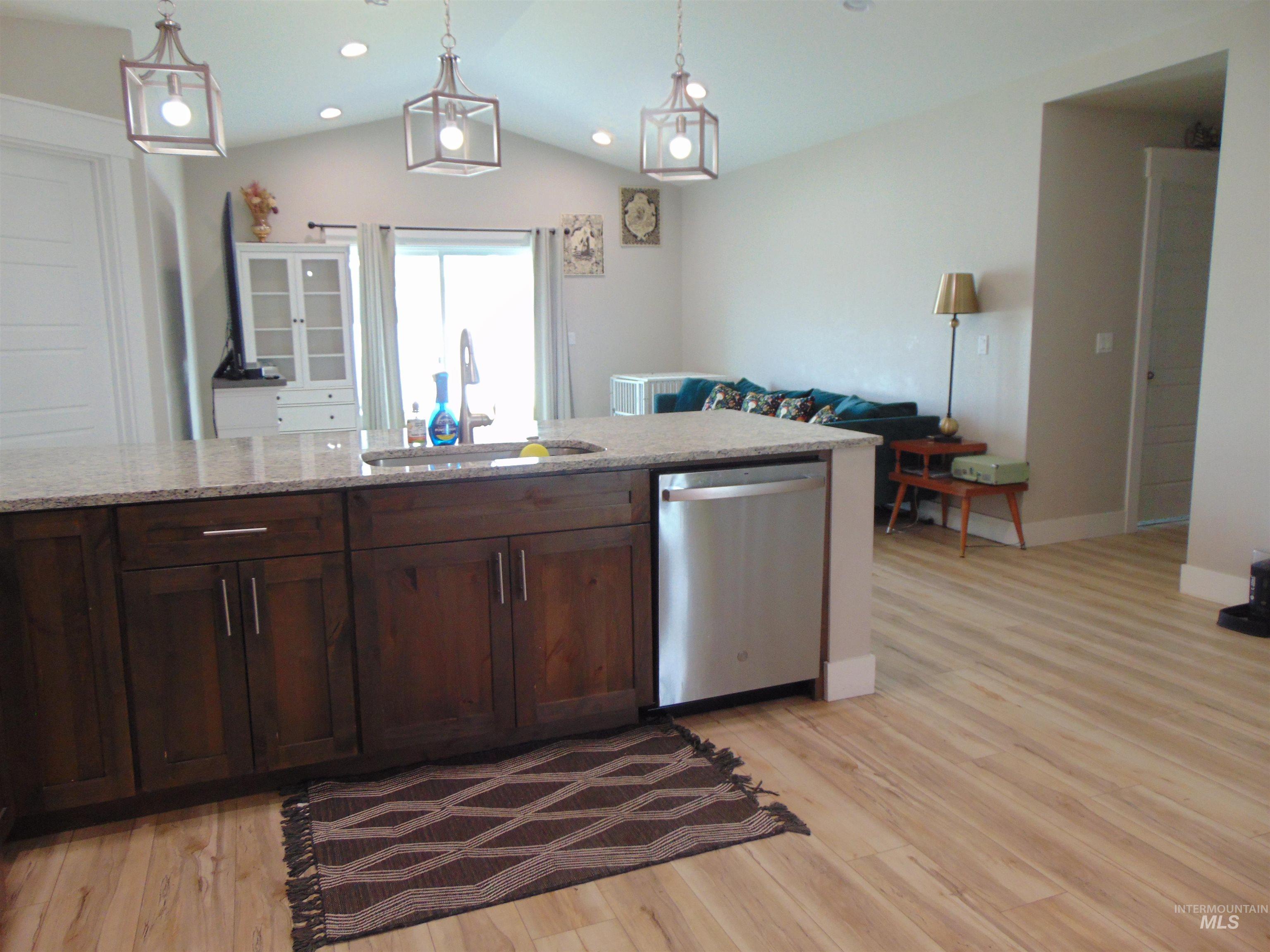 901 Campbell Street Vale, OR 97918 - Photo 8 of 22 Kitchen with stainless steel dishwasher, dark wood finish cabinetry, light stone counters, light wood finished floors, and vaulted ceiling