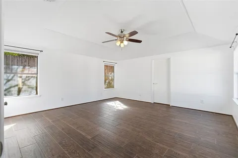 an empty room with wooden floor chandelier fan and windows