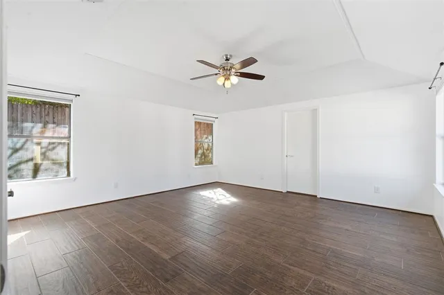 an empty room with wooden floor chandelier fan and windows