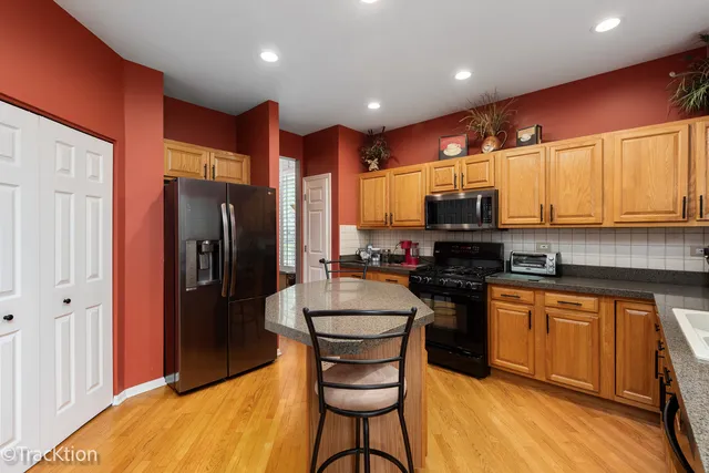 a kitchen with stainless steel appliances granite countertop a refrigerator a stove top oven and a sink with wooden floor