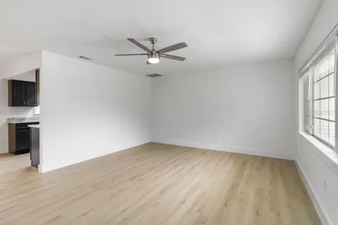 an empty room with wooden floor fan and windows