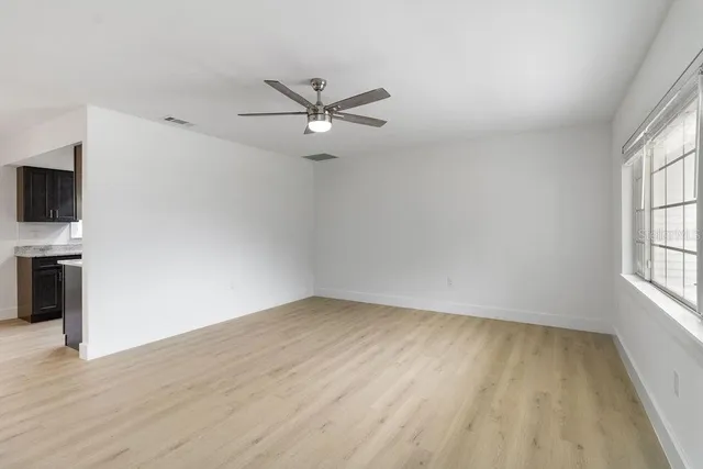 an empty room with wooden floor fan and windows