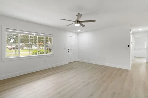an empty room with wooden floor ceiling fan and windows