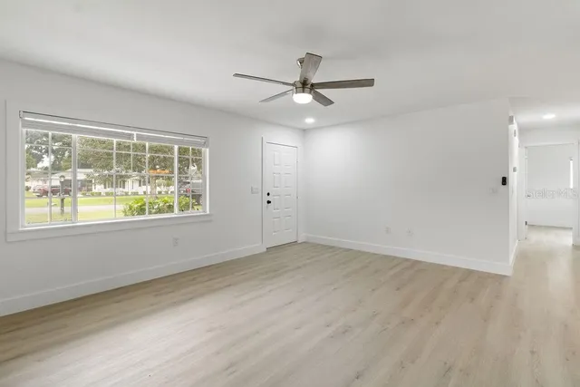 an empty room with wooden floor ceiling fan and windows