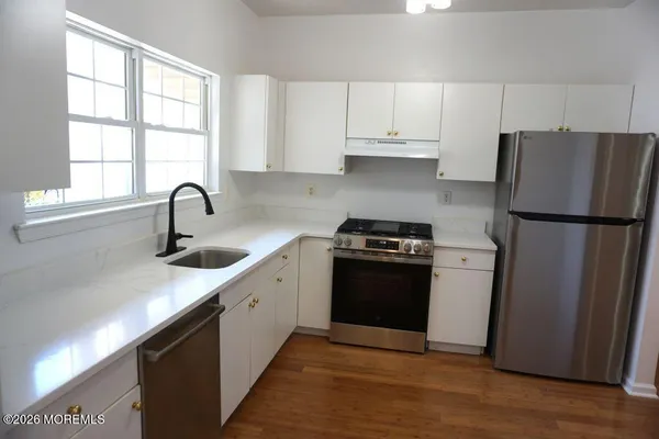 a kitchen with white cabinets appliances a sink and a window