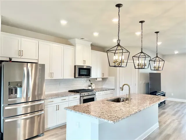 a kitchen with stainless steel appliances granite countertop a sink a stove a refrigerator and island with wooden floor