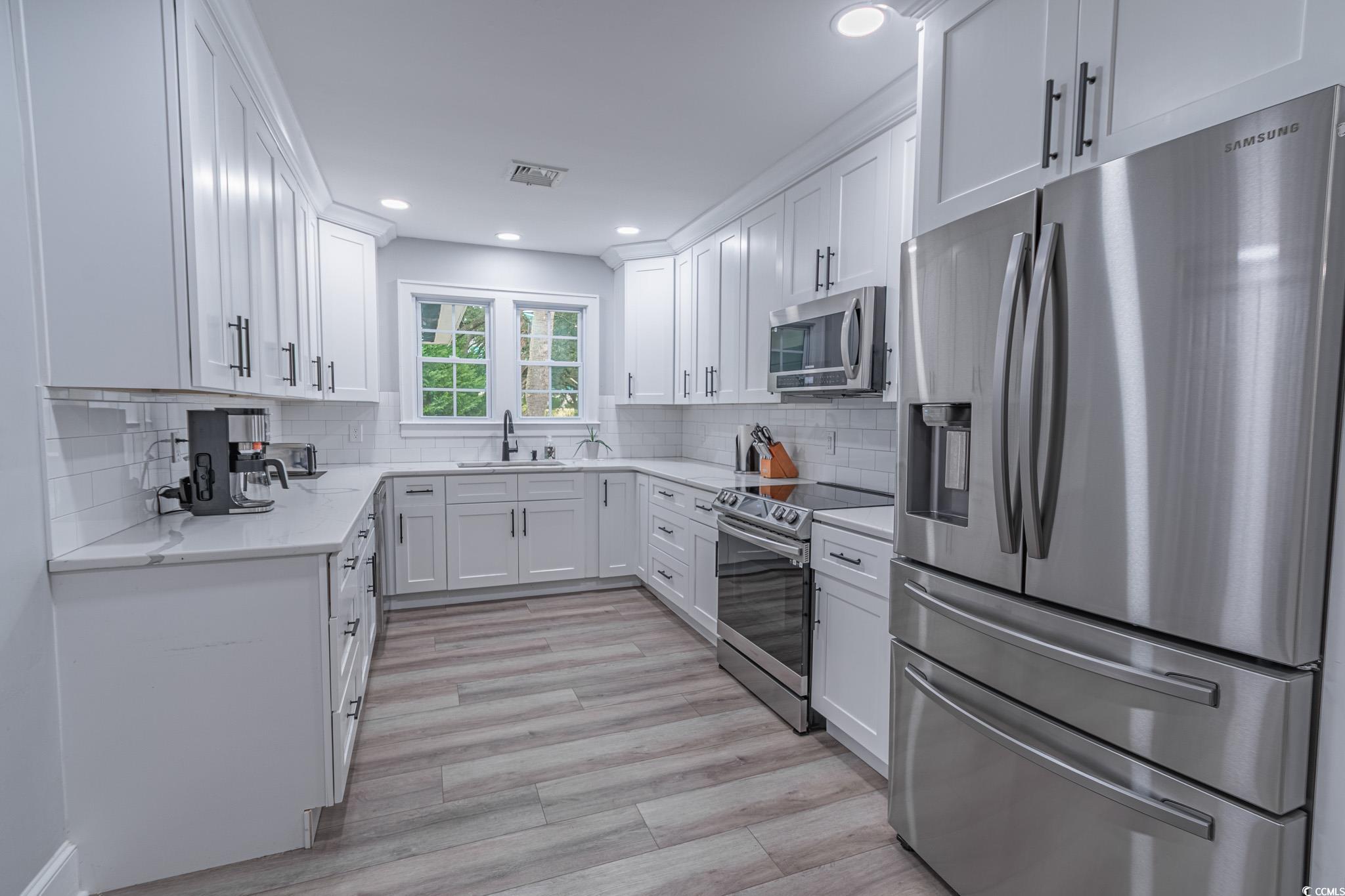 5307 North Ocean Boulevard Myrtle Beach, SC 29577 - Photo 13 of 39 Kitchen featuring appliances with stainless steel finishes, white cabinets, light stone countertops, recessed lighting, and light wood-type flooring