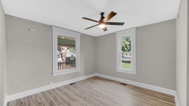 an empty room with wooden floor windows and ceiling fan