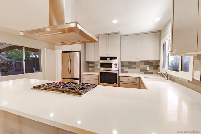 a kitchen with stainless steel appliances kitchen island granite countertop a stove a sink a refrigerator and white cabinets with wooden floor