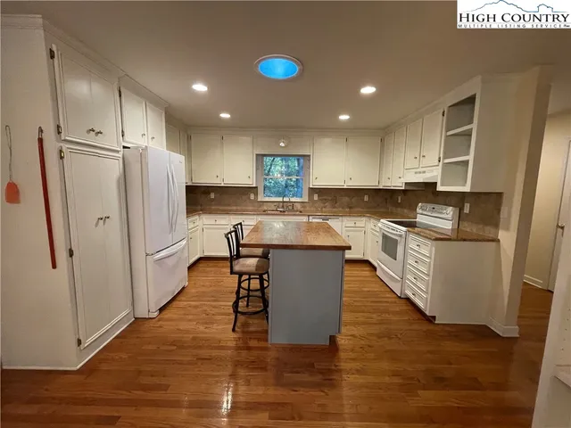 a kitchen with granite countertop a refrigerator oven a sink dishwasher and white cabinets with wooden floor