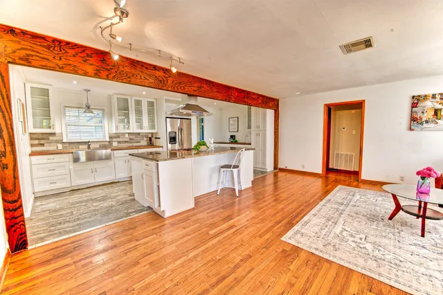 a living room with stainless steel appliances kitchen island granite countertop a refrigerator stove oven and white cabinets with wooden floor