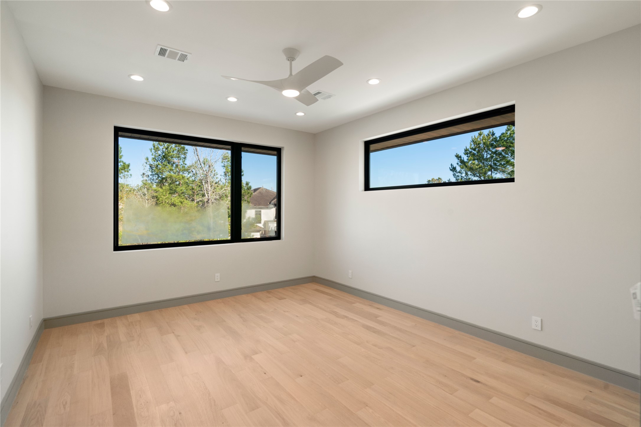 47 Pronghorn Place Spring, TX 77389 - Photo 27 of 44 This room offers a bright and airy space with light wood floors, neutral walls, and large windows providing natural light and green views. Modern ceiling fan and recessed lighting enhance the fresh, contemporary feel.