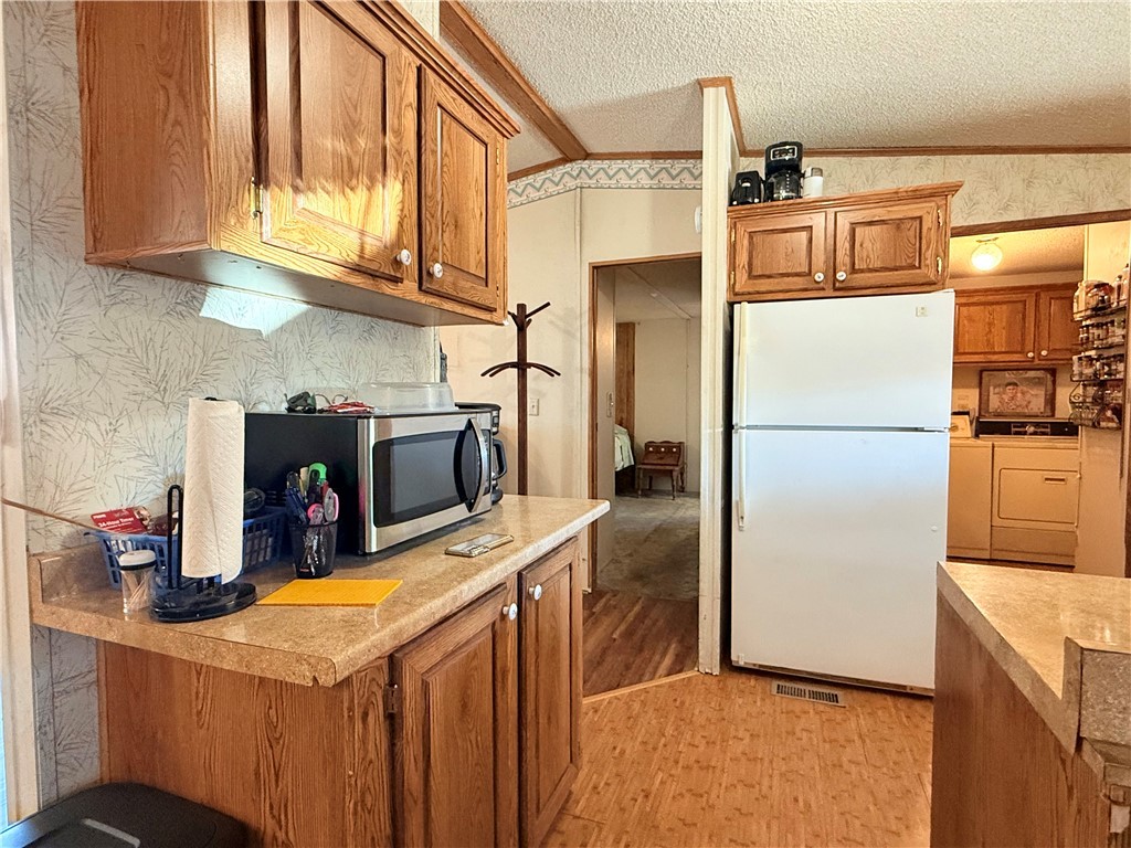 1637 Talc Road Bullhead City, AZ 86442 - Photo 13 of 37 Kitchen featuring freestanding refrigerator, wallpapered walls, a textured ceiling, brown cabinetry, and separate washer and dryer