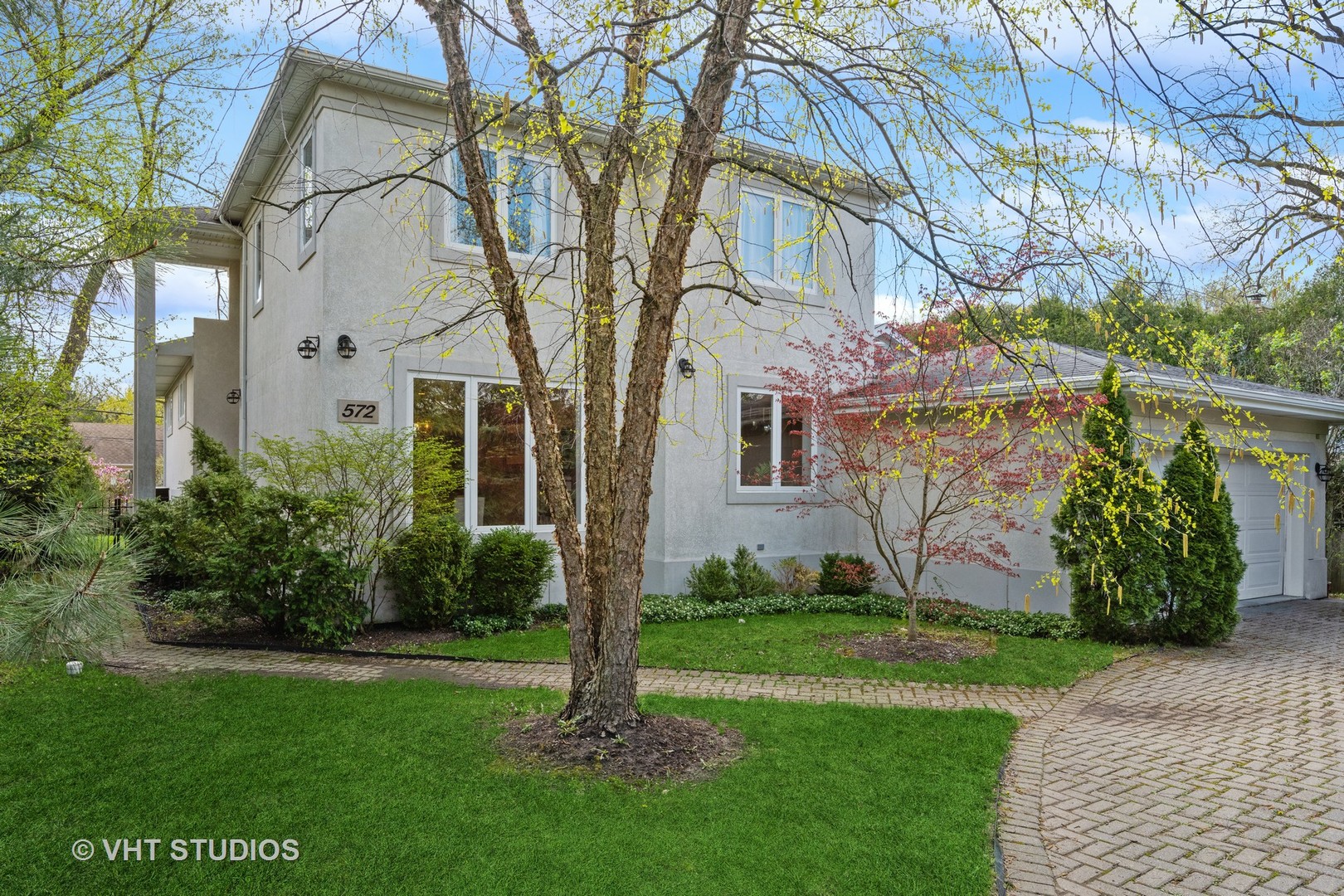 a view of a white house next to a yard with big trees