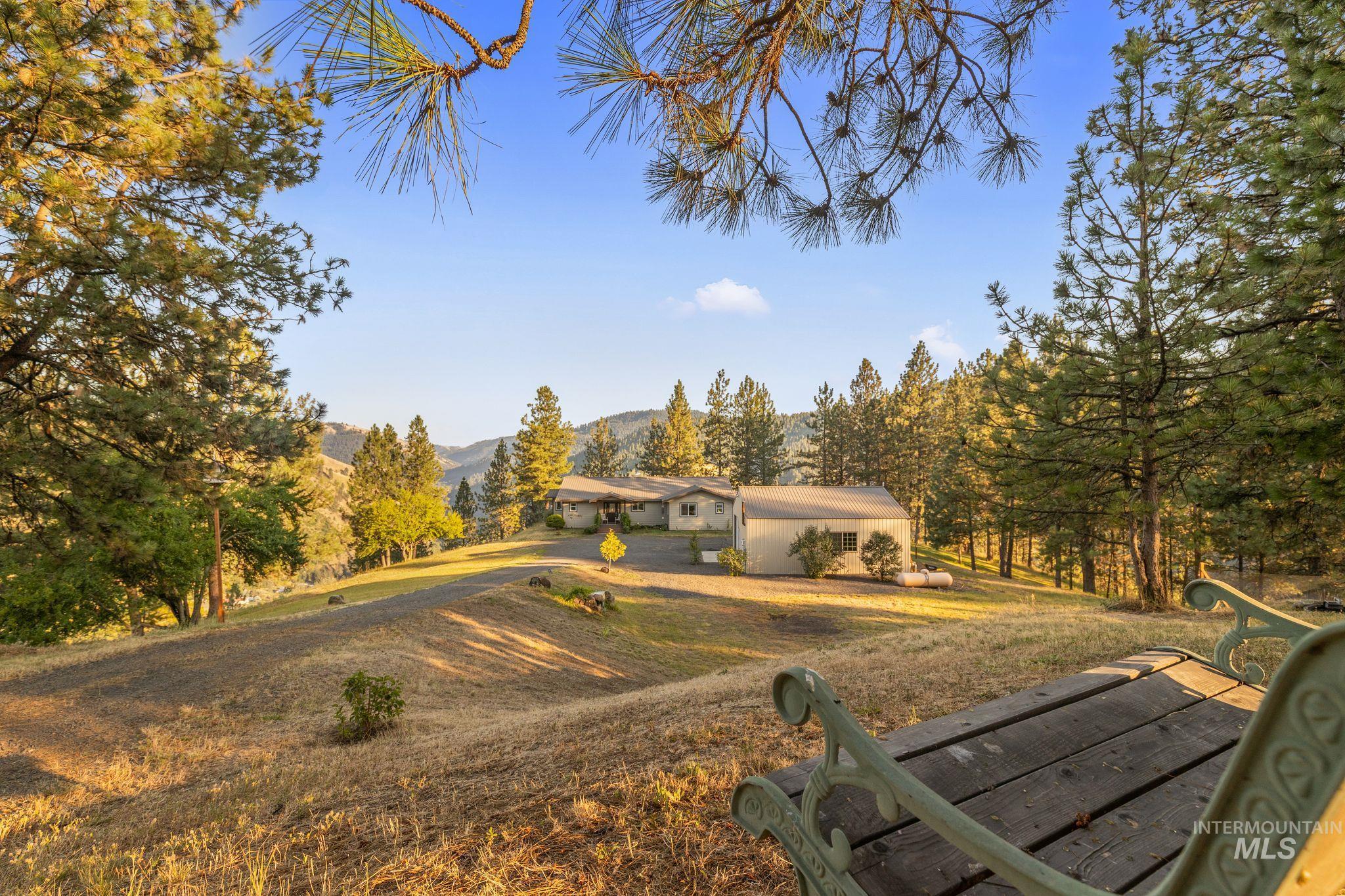 435 River Pointe Lane Lenore, ID 83541 - Photo 41 of 50 Expansive property featuring a gravel driveway, a single-story residence, a detached auxiliary building, mature evergreen trees, and a mountain backdrop