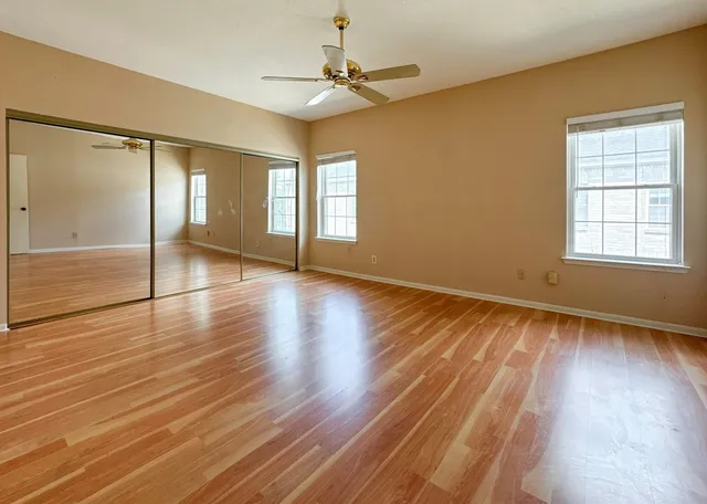 an empty room with wooden floor fan and windows