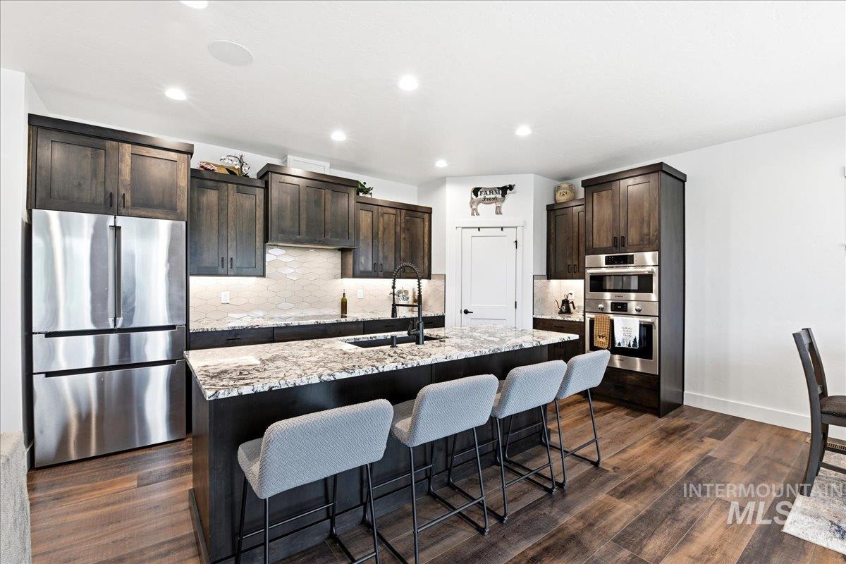 13152 Hawks Bay Road Donnelly, ID 83615 - Photo 8 of 29 Modern kitchen featuring dark wood cabinetry, stainless steel appliances, speckled stone countertops, and wood-finish flooring