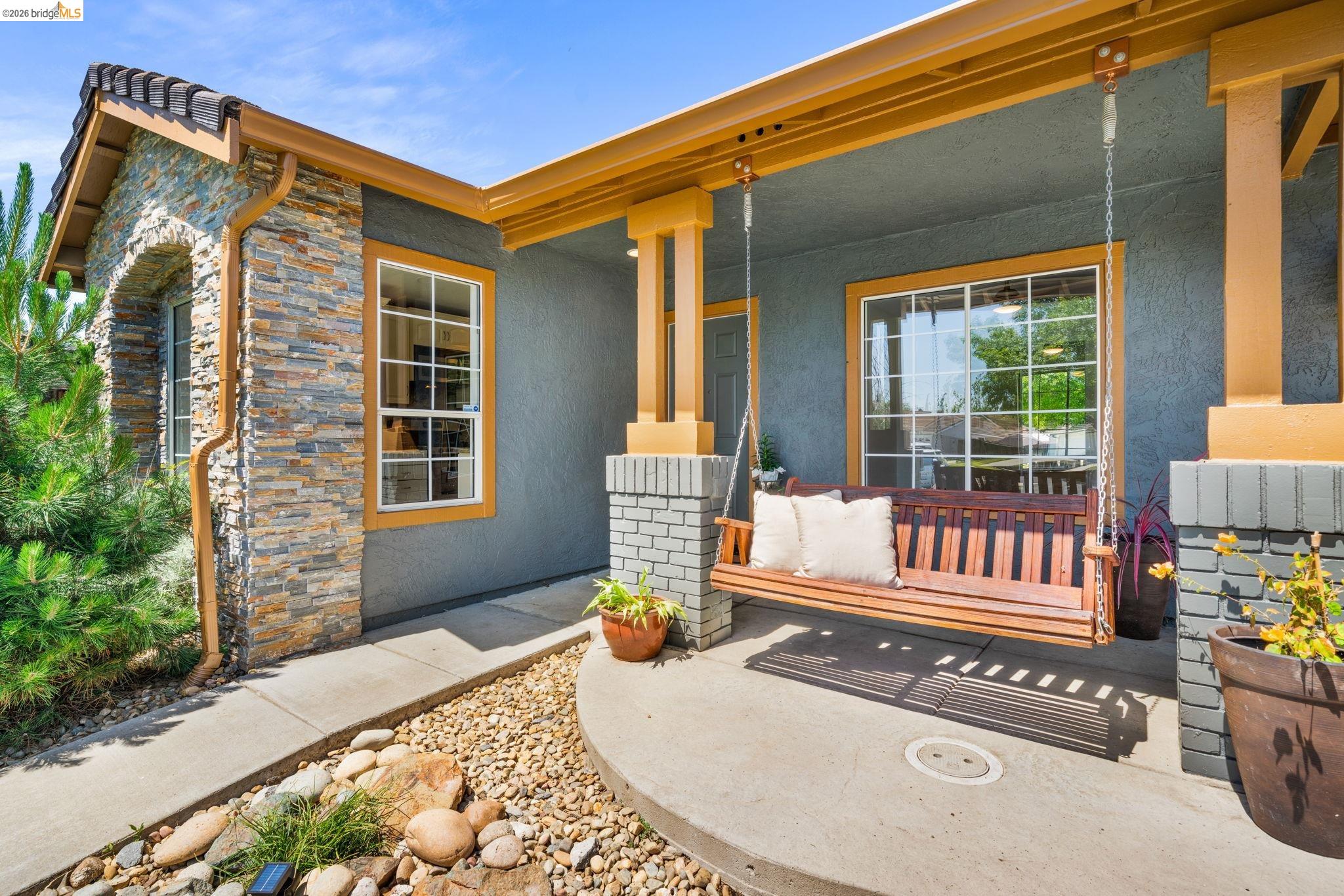 1186 El Rio Court Livermore, CA 94551 - Photo 3 of 60 Inviting front porch featuring a wood-finish porch swing, a stucco exterior, and stacked stone accents