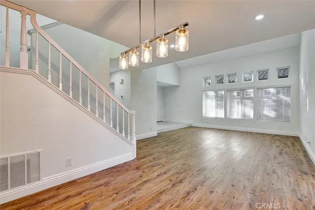 an empty room with wooden floor chandelier and windows