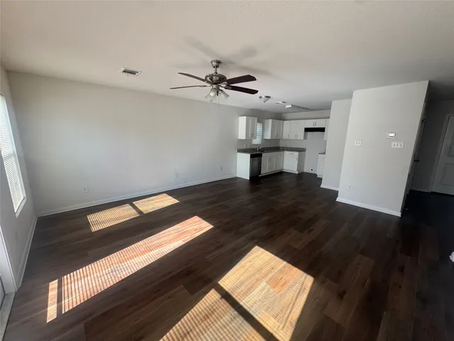 a view of an empty room with wooden floor and a ceiling fan
