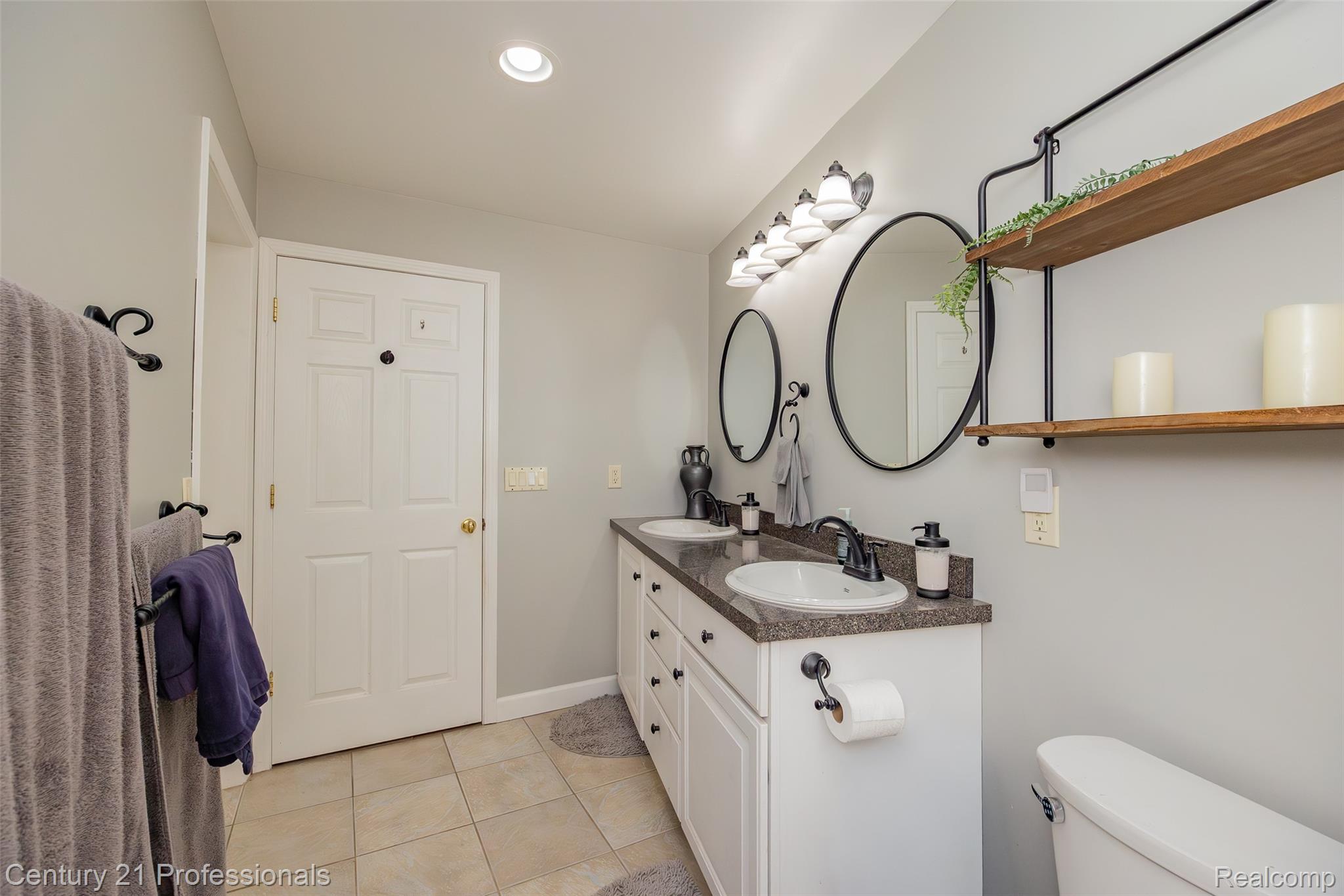 3251 Mann Road Clarkston, MI 48346 - Photo 22 of 40 Dual vanity with dark countertops, two oval mirrors, and a six-light fixture
