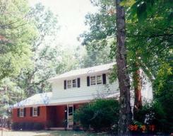 a view of house with outdoor seating and covered with trees