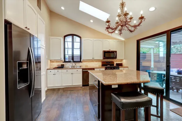 a kitchen with stainless steel appliances granite countertop a refrigerator a sink dishwasher a stove and a dining table with wooden floor