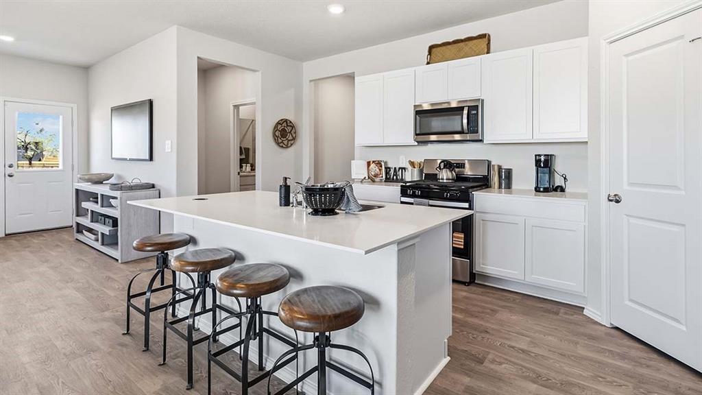 226 Pheasant Run Road Terrell, TX 75160 - Photo 29 of 36 Kitchen featuring white cabinetry, stainless steel appliances, a center island with countertop seating, and wood-finish flooring
