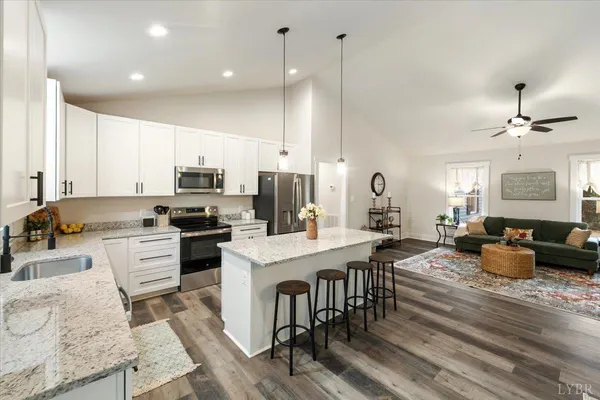 a kitchen with stainless steel appliances granite countertop a stove a sink dishwasher a refrigerator and white cabinets with wooden floor