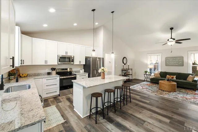 a kitchen with stainless steel appliances granite countertop a stove a sink dishwasher a refrigerator and white cabinets with wooden floor