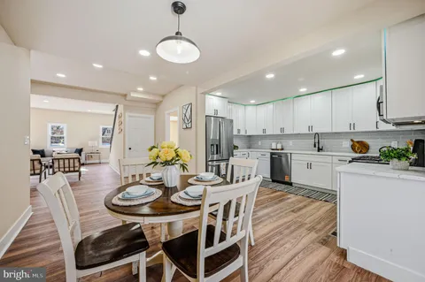 a kitchen with stainless steel appliances kitchen island granite countertop a dining table chairs and white cabinets