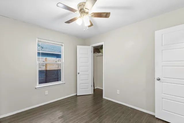 an empty room with wooden floor chandelier fan and windows