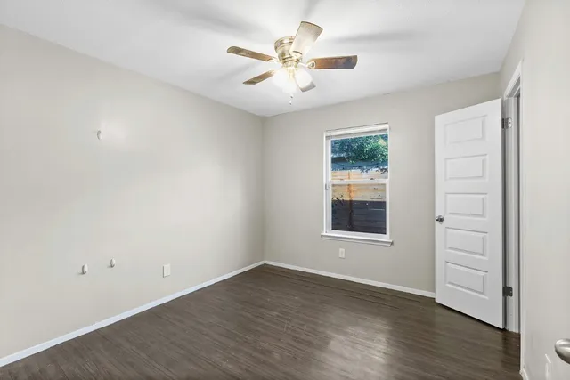 an empty room with wooden floor ceiling fan and windows