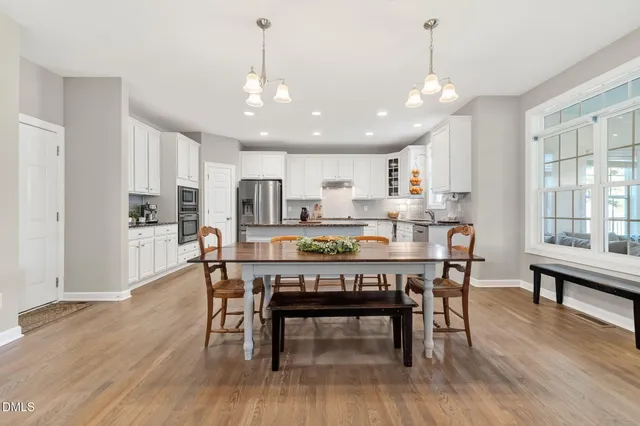 a kitchen with a dining table chairs wooden floor cabinets and appliances