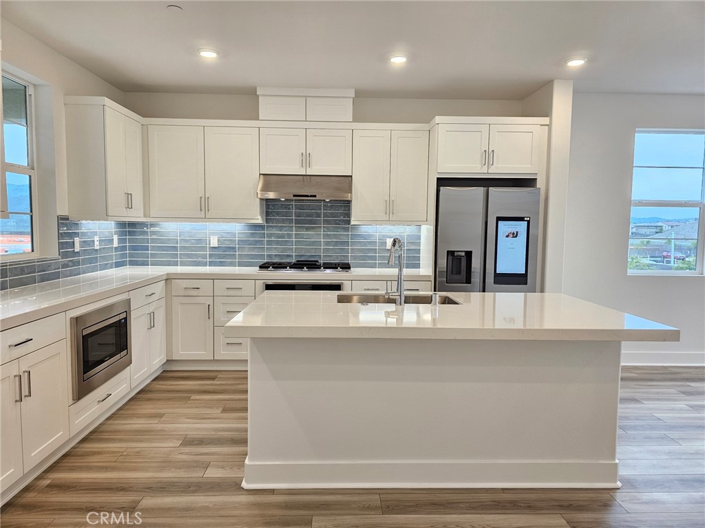 a kitchen with kitchen island granite countertop a stove top oven a sink dishwasher and white cabinets with wooden floor