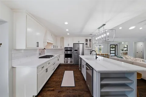 a large kitchen with kitchen island a stove a sink a refrigerator and a dining table with wooden floor