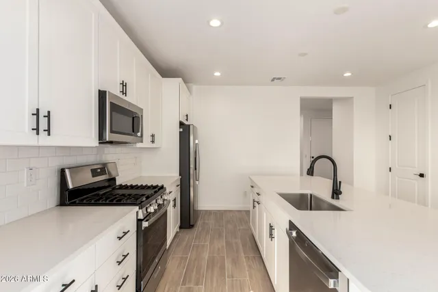 a kitchen with stainless steel appliances granite countertop a refrigerator a stove a sink a dining table and chairs with wooden floor