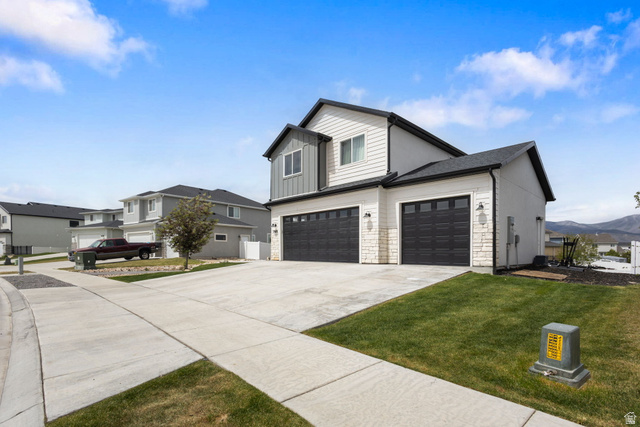 7889 Bristlecone Road Eagle Mountain, UT 84005 - Photo 2 of 42 Contemporary home exterior featuring a third-car garage with dark paneled doors, white siding, and stone accents