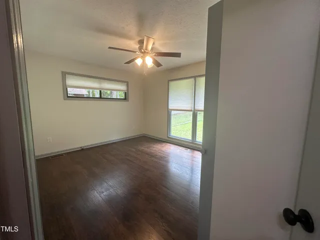 an empty room with wooden floor fan and windows