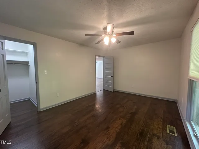 an empty room with wooden floor fan and windows