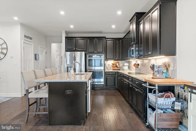 a kitchen with stainless steel appliances kitchen island granite countertop a stove a sink dishwasher and a refrigerator with wooden floor