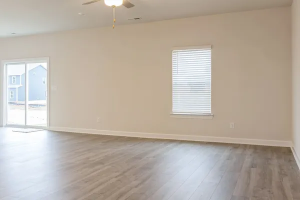 an empty room with wooden floor chandelier fan and windows